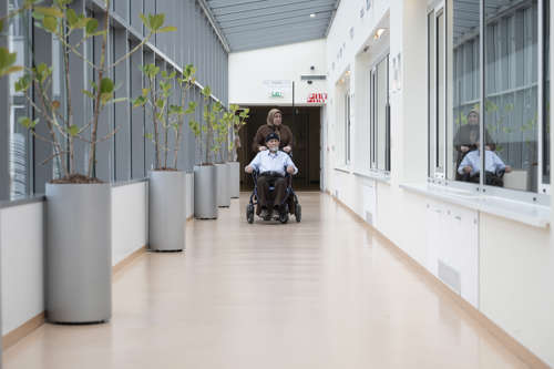 Naaste duwt patiënt in rolstoel door lange gang