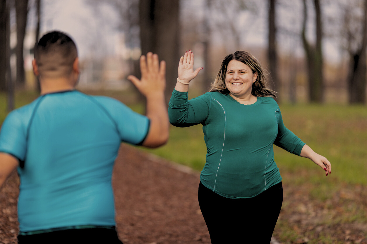 Foto van twee sportende mensen met obesitas die elkaar een high five geven
