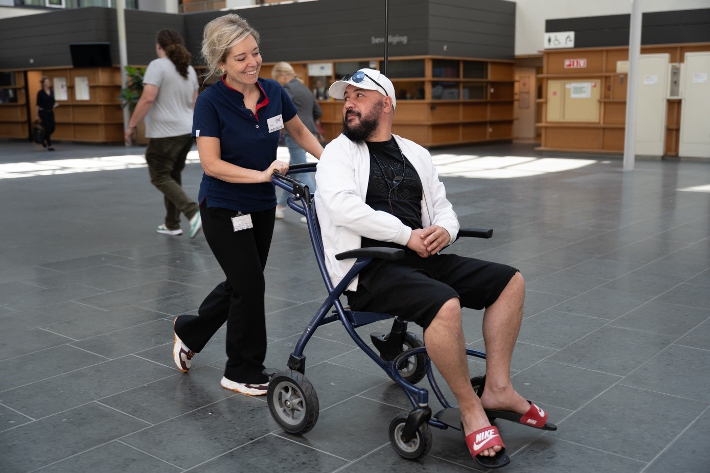 Een vrijwilliger begeleidt patiënt in een rolstoel naar de polikliniek